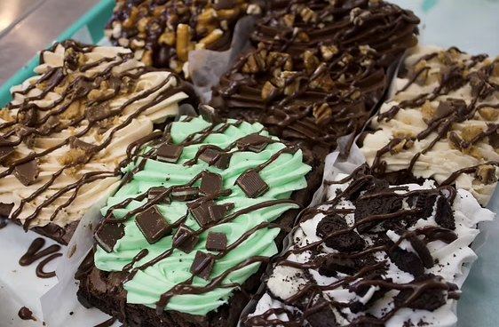 Thick brownies topped with swirled frostings, chocolate chunks, and chocolate drizzle
