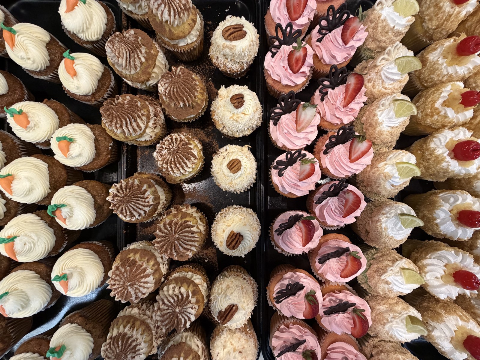 Trays of carrot, tiramisu, coconut, strawberry, key lime, and cannoli cupcakes