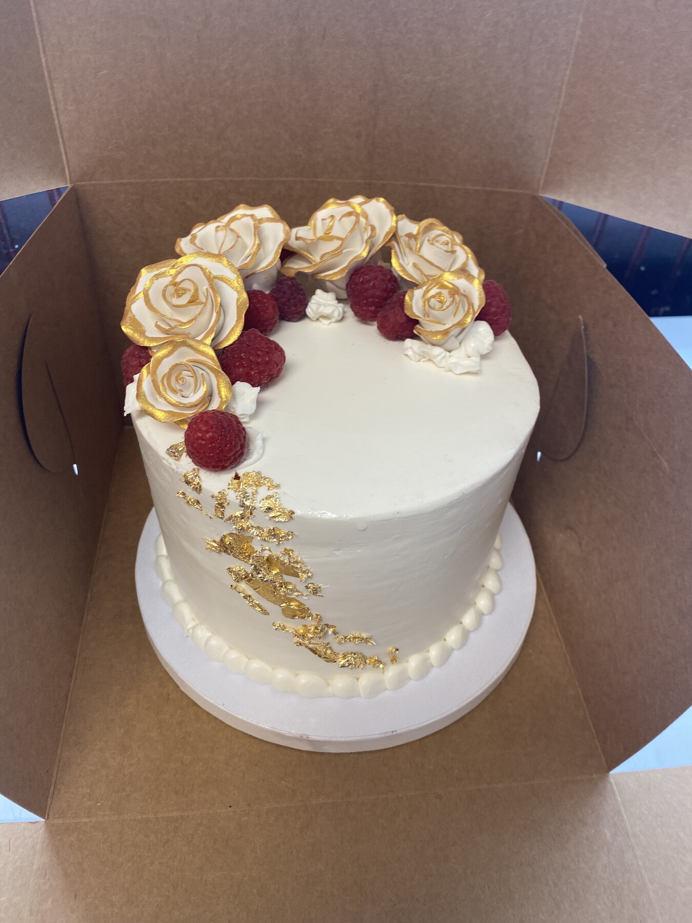 White buttercream cake with gold-brushed sugar roses, fresh raspberries, and gold leaf