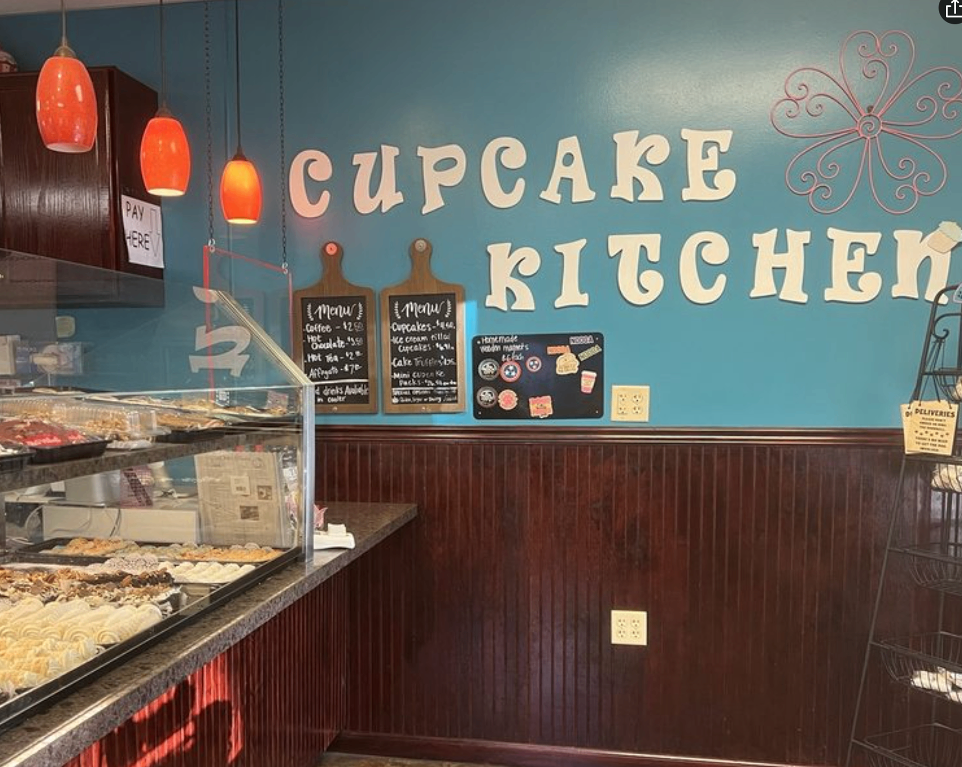 Cupcake Kitchen interior with teal wall, hand-painted logo, chalkboard menus, and hanging orange pendant lights