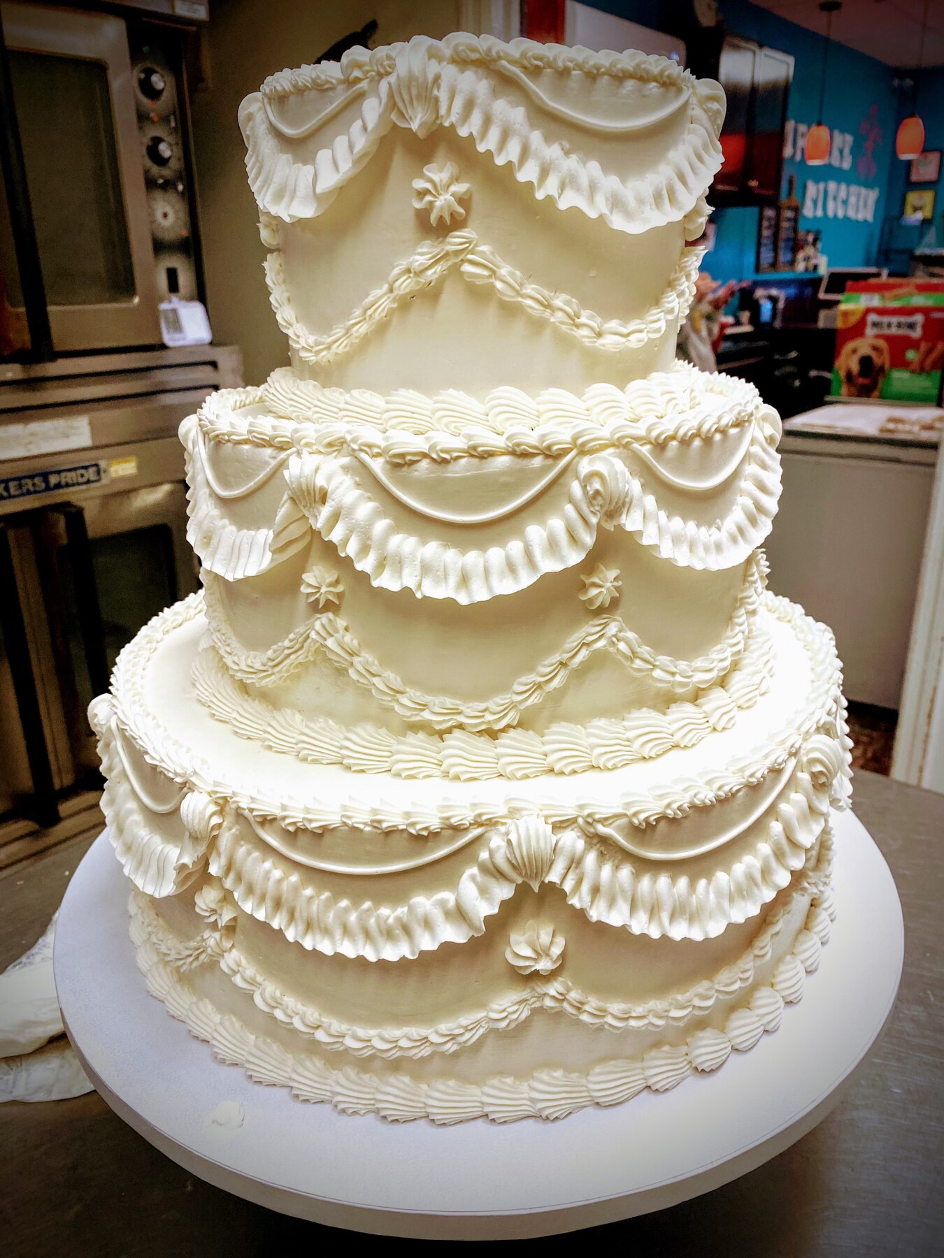 Three-tier ivory wedding cake with hand-piped drapes, ruffles, and shell borders