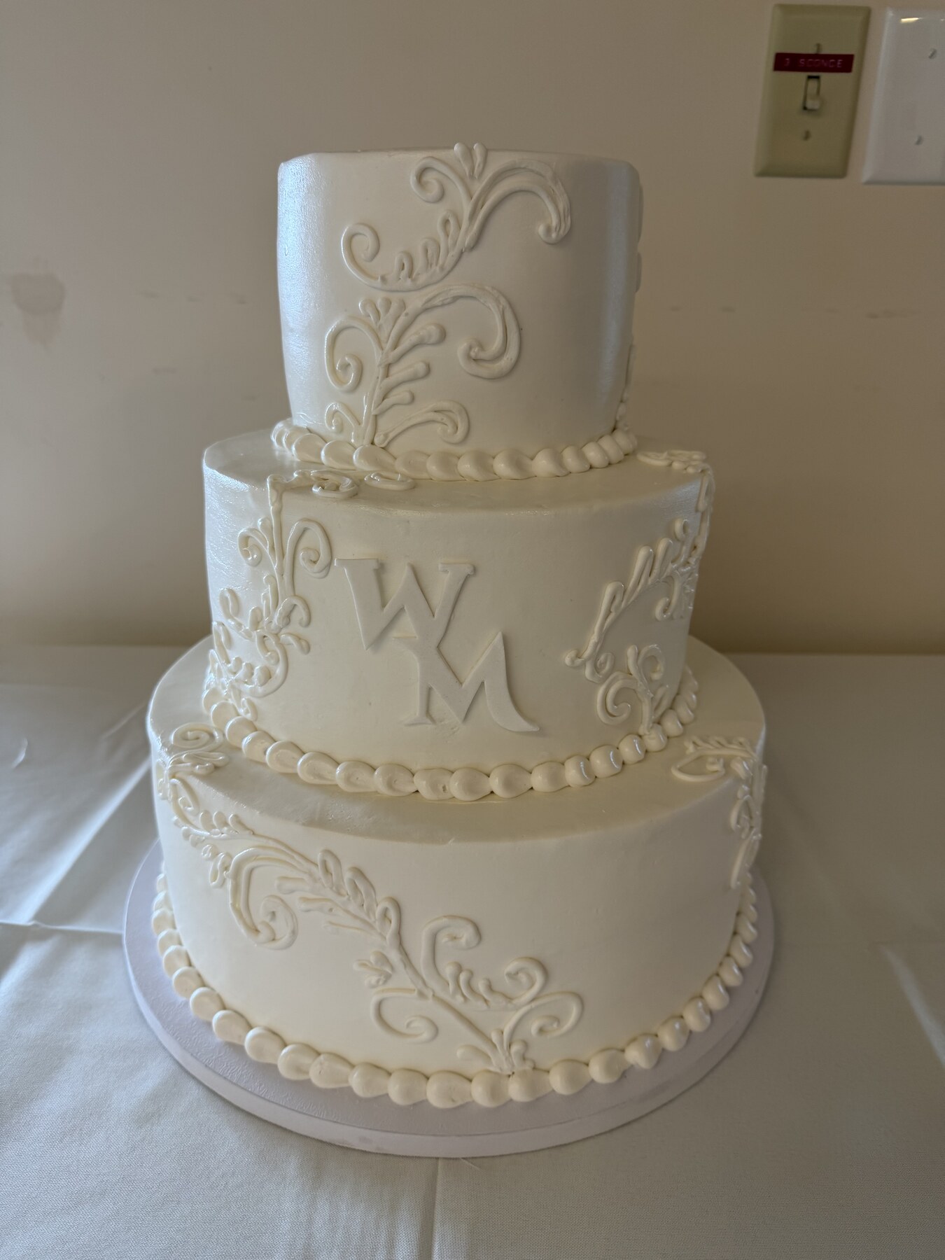 Three-tier white wedding cake with piped scrollwork and a monogram