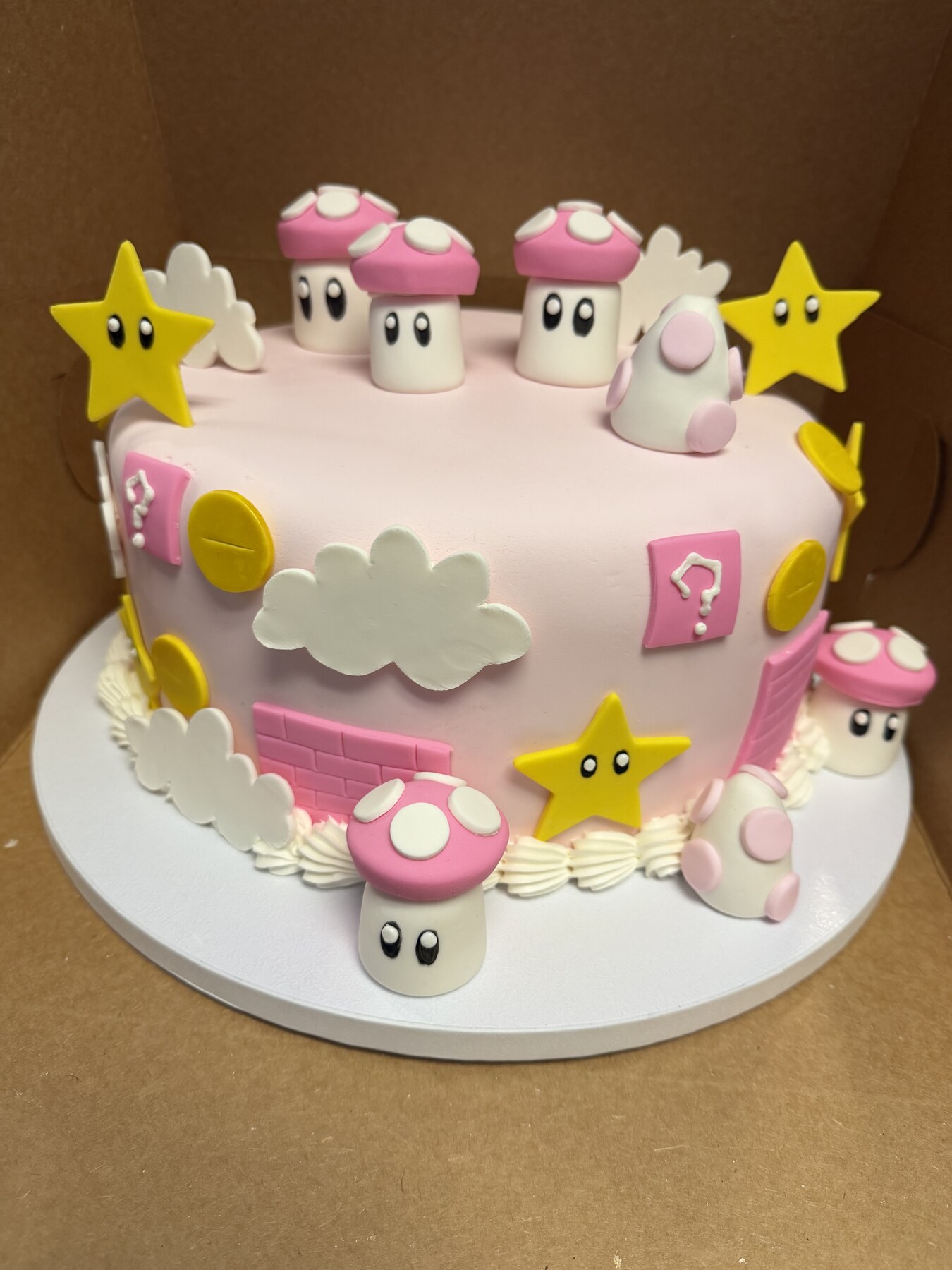 Pink fondant video game themed birthday cake with mushrooms, stars, and clouds